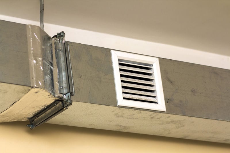 Ventilation pipes in silver insulation material hanging from the ceiling inside new building.